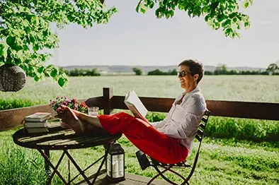 Frau sitzt mit Buch auf einer Terrasse vor weiter Landschaft – ruhige und inspirierende Atmosphäre.