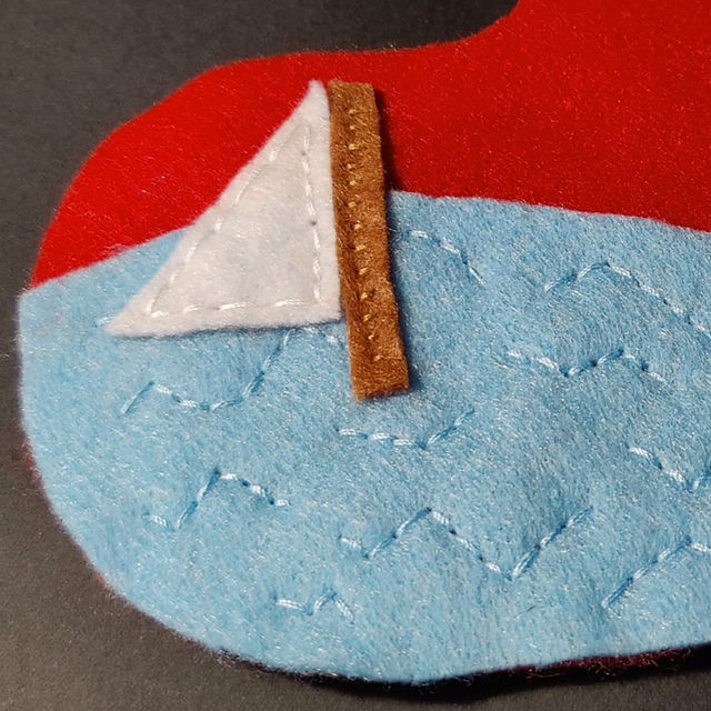 Blue felt sea on red background. Felt ship's mast and sail set on the sea. 