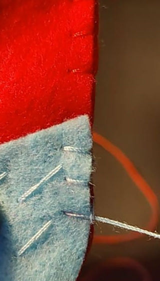 Close-up of red and blue felt pieces stitched together with white thread.