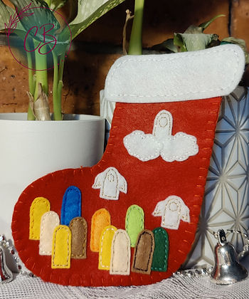 Felt Christmas stocking with colourful motifs, set against a brick wall. Silver bell and plant in the background, cosy ambiance.