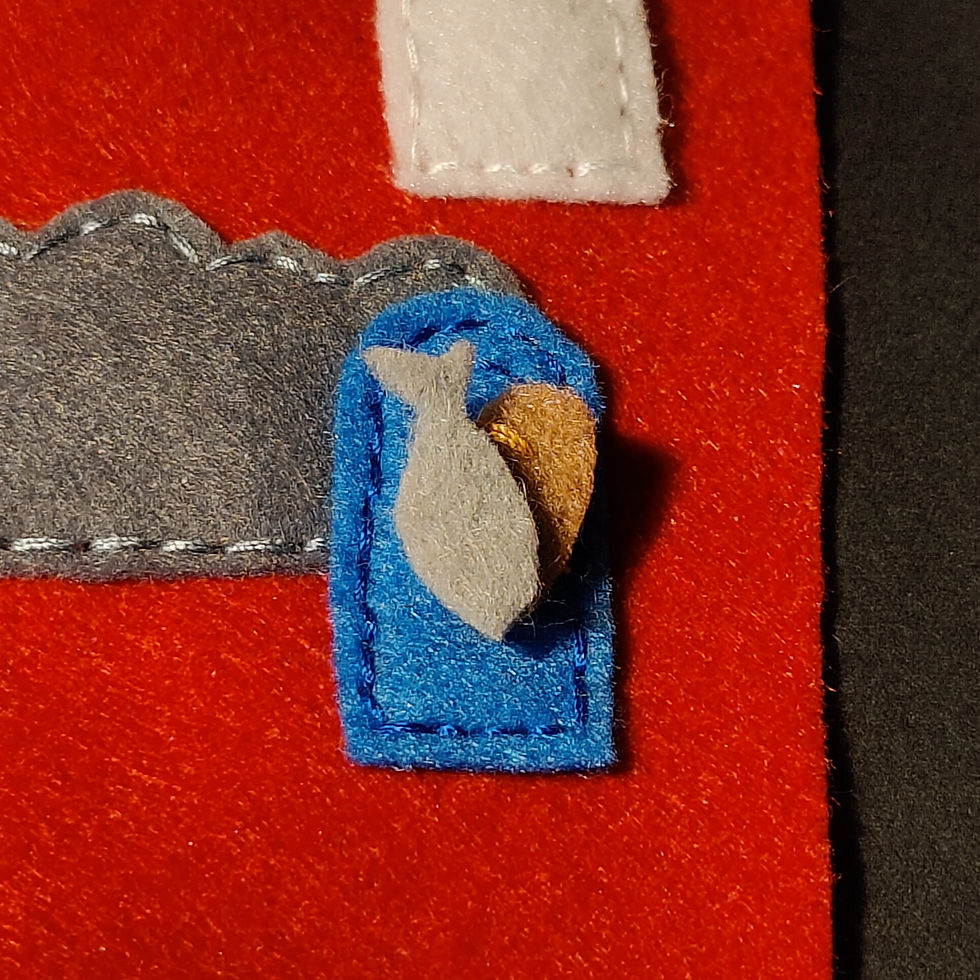 Felt fish and heart on blue patch, red background. White and gray felt pieces add texture, creating a cosy, handmade feel. No text visible.