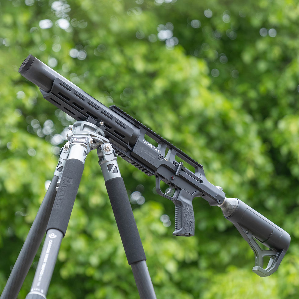 A Kral Puncher K rifle with a wooden stock and scope leans against a tree amid greenery. The setting is a lush outdoor environment, conveying tranquility.