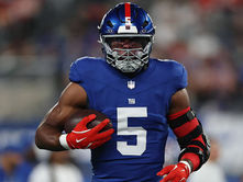 New York Giants edge rusher Kayvon Thibodeaux (5) in a blue Giants jersey and helmet, carrying a football while wearing red gloves