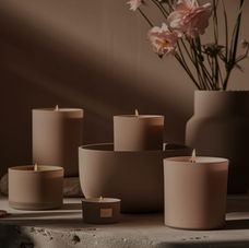 5 lit candles of varying sizes with a flower vase and flowers in the background, all set in a moody ambiance.