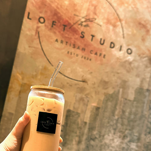 Hand holding up a cup of ice coffee against a wall decorated with the loft studio artisan cafe logo.