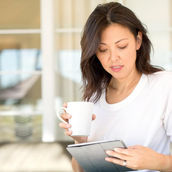 a woman looking at her ipad and holding coffee in her hand