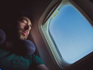 a young man sleeping with a travel pillow during a flight