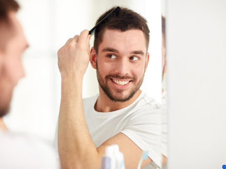 a young man brushing his hair and looking at a mirror