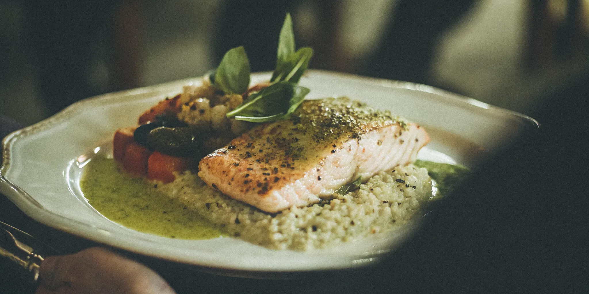 Plated grilled salmon with lemon-herb sauce, roasted vegetables, and couscous on elegant dinnerware