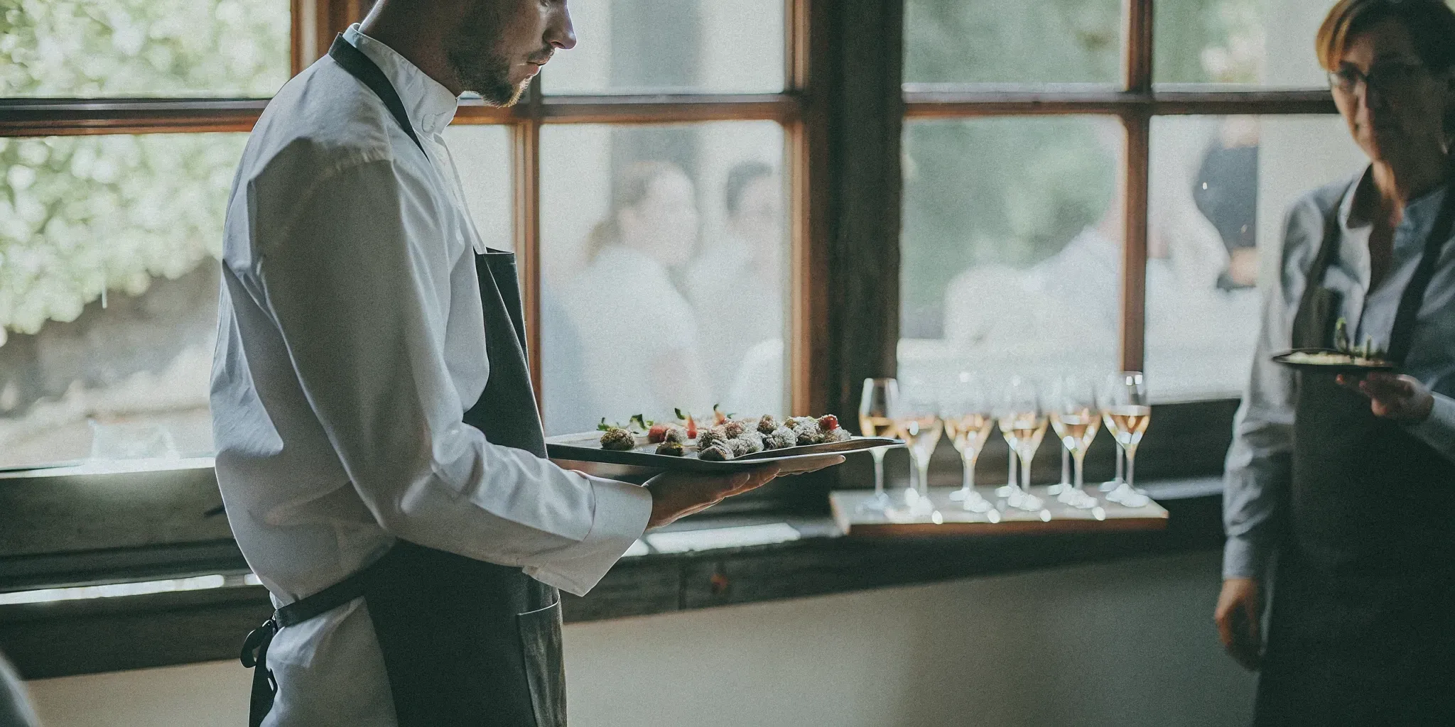 Chef presenting a plated tasting dish to a couple during a wedding catering tasting session in a bright San Diego venue