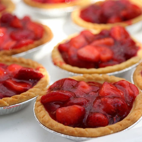 Strawberry Festival in Niagara-on-the-Lake. Mini strawberry tarts with glossy red filling on a white tray, close-up of several bite-sized pies in foil cups.