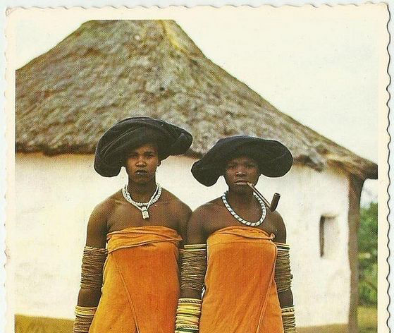 Two Xhosa women next to their rondavel