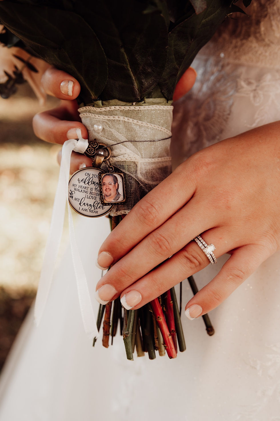 a bride holding her bouquet showing personal charms that are wrapped into the ribbon of the bouquet to honor a loved one that has passed