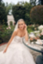A bride wearing a strapless lace bridal gown sitting outside in a garden with flowers and tea dishes set out