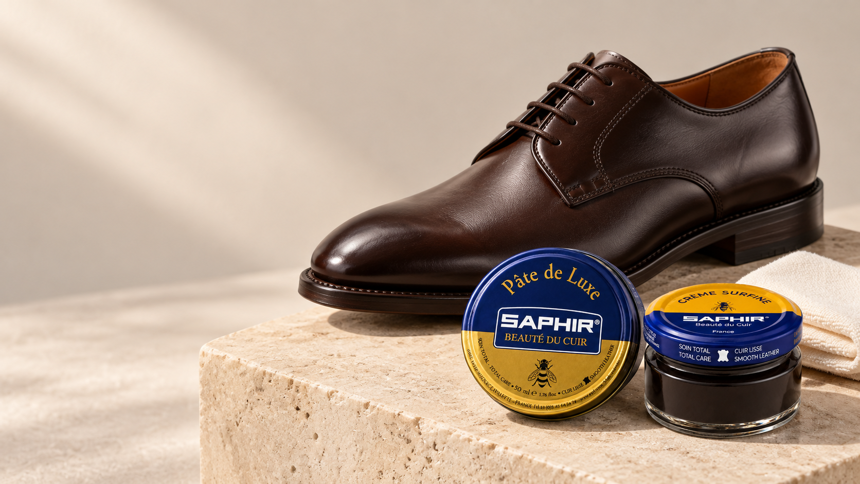 Saphir Crème Surfine and Pâte de Luxe beside a dark brown derby on warm limestone