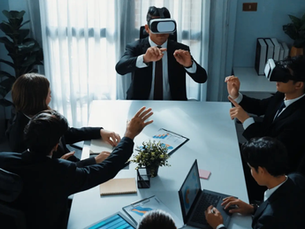 A group in suits at a table uses VR headsets, gesturing mid-air. Laptops, charts visible. Bright room with plants, creating a tech-focused mood.
