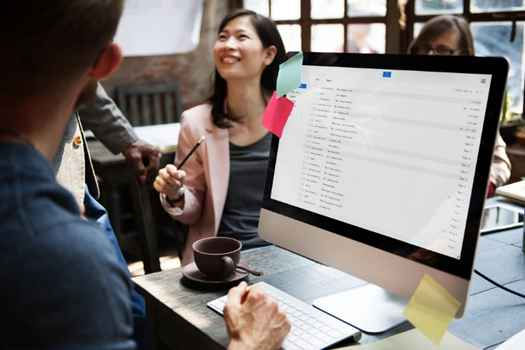 People in a casual office setting discussing near a screen displaying emails. One person is smiling, creating a collaborative, positive mood.