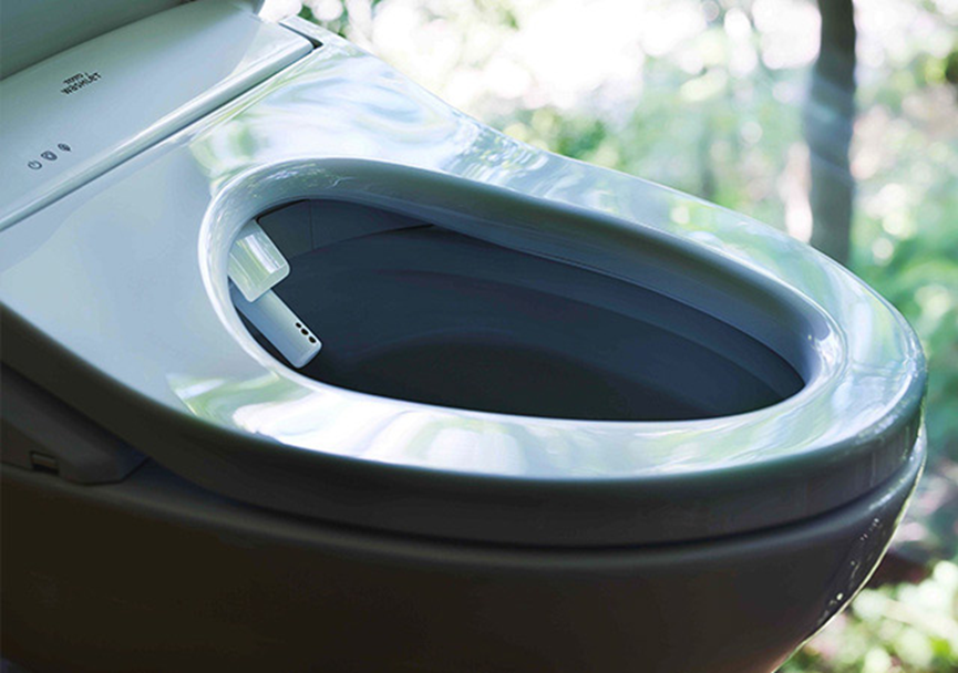 A modern bidet toilet with a built-in nozzle in a bright setting, surrounded by blurred green foliage, exudes a sleek and clean look.