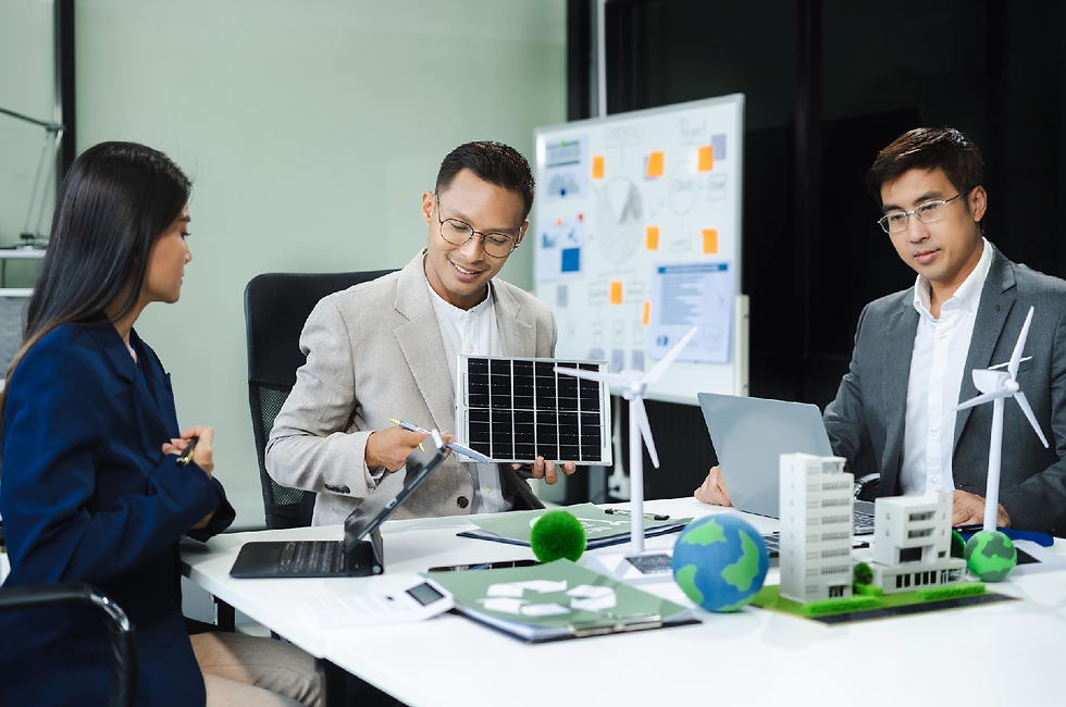 Three people in a meeting room discuss sustainable energy, holding models of a solar panel and wind turbine. A whiteboard with diagrams is behind them.