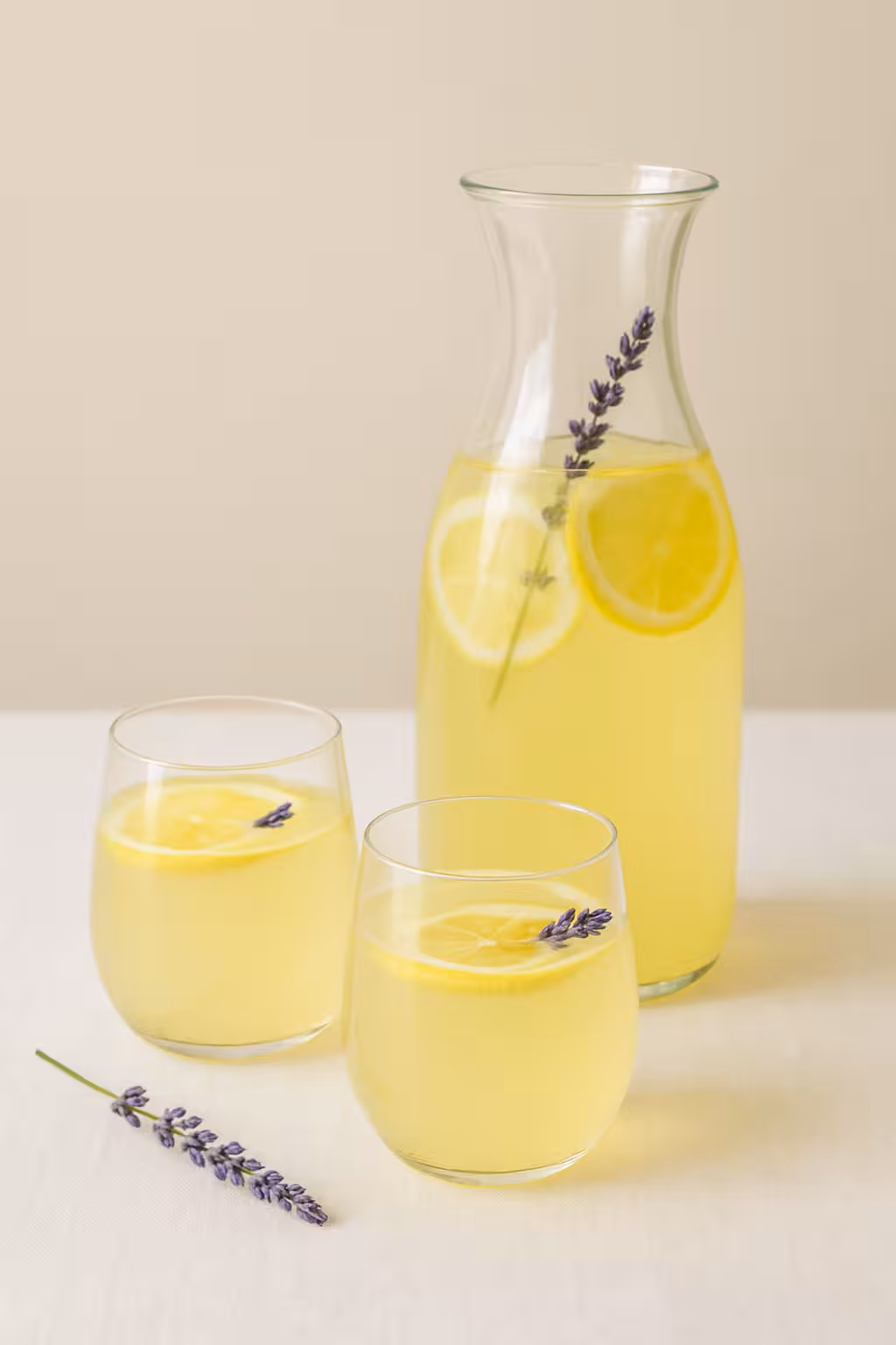 Dilimlenmiş limon ve lavanta çiçekleriyle süslenmiş lavantalı limonata bardağı.