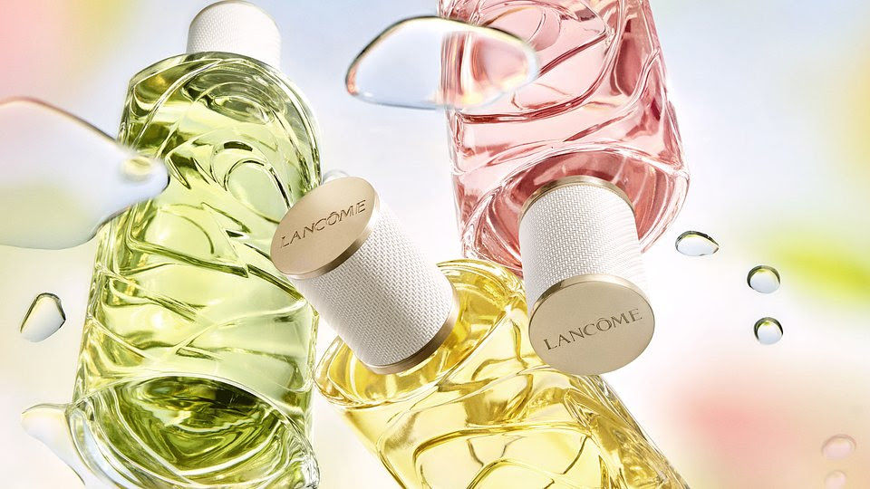 Frascos de perfume coloridos (verde, rosa, amarelo) com tampas brancas "Lancôme". Fundo pastel com gotas de água. Atmosfera fresca e vibrante.