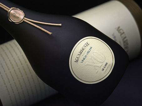 Garrafa de aguardente Vinha Velha XO preta com selo dourado sobre fundo escuro. Texto visível na etiqueta: "18/10.000 garrafas".