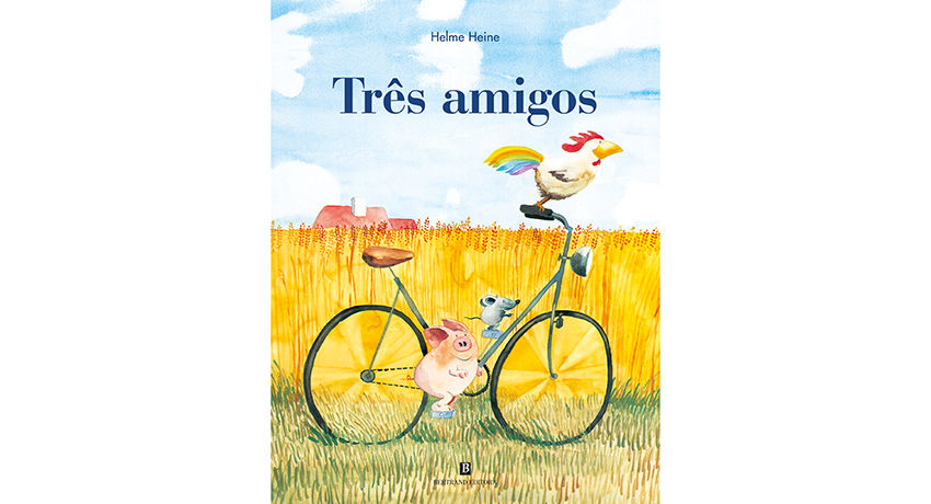 Capa do livro "Três Amigos" de Helme Heine. Um galo, um rato e um porco compartilham uma bicicleta em um campo de trigo sob céu azul.
