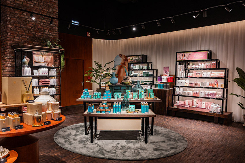 Loja de cosméticos com prateleiras cheias de produtos em tons pastel. Mesa central com itens azuis. Ambiente elegante com luz suave.