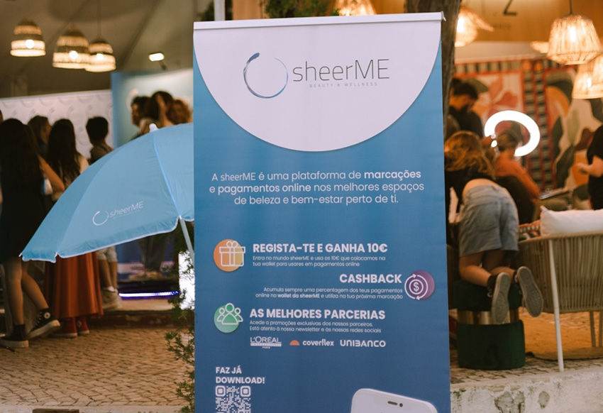Banner shearME azul em evento ao ar livre com pessoas ao fundo. Texto destaca plataforma e parcerias. Guarda-chuva shearME visível. Atmosfera animada.