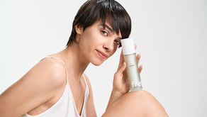 Mulher de cabelo curto sorri enquanto segura um frasco transparente de creme "fresh" em fundo branco. Veste roupa branca, transmitindo leveza.