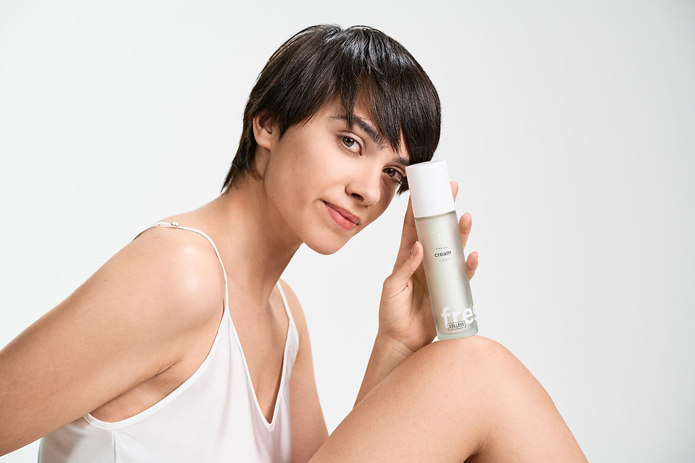 Mulher de cabelo curto sorri enquanto segura um frasco transparente de creme "fresh" em fundo branco. Veste roupa branca, transmitindo leveza.