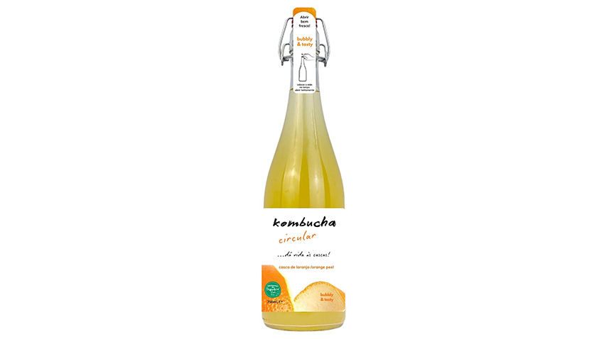 Garrafa de kombucha com tampa flip-top. Rótulo com texto: "circular, casca de laranja." Líquido amarelo. Fundo branco minimalista.
