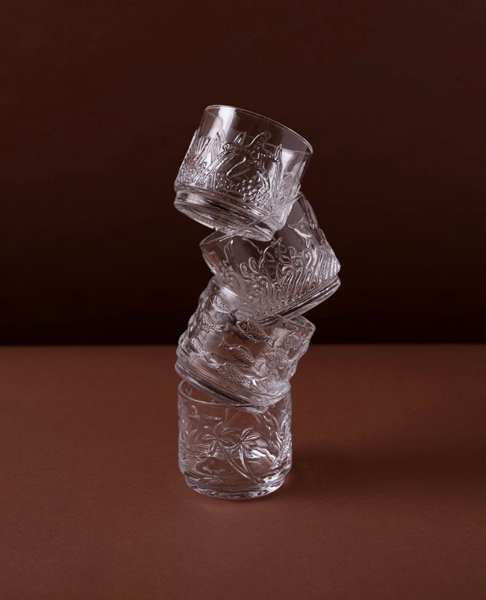 "Three stacked transparent glasses balanced artistically over a brown background."