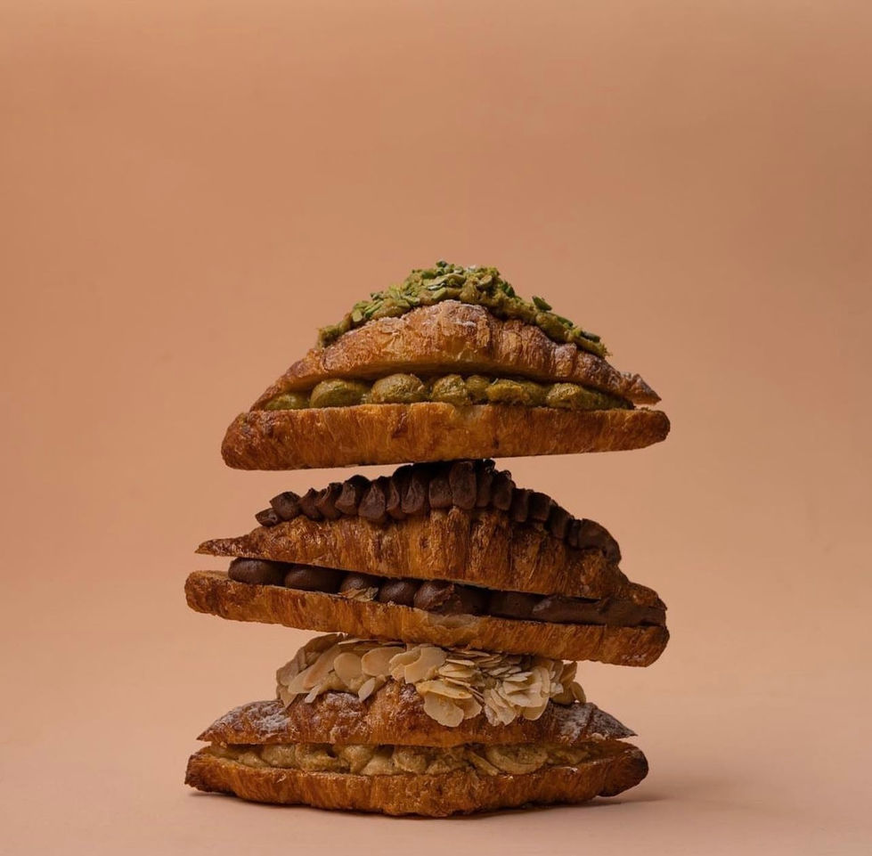"Stack of golden croissants topped with pistachios and almond flakes against beige background."