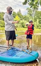 Father and son on a paddleboard river trip, with the child proudly holding a fish he caught.