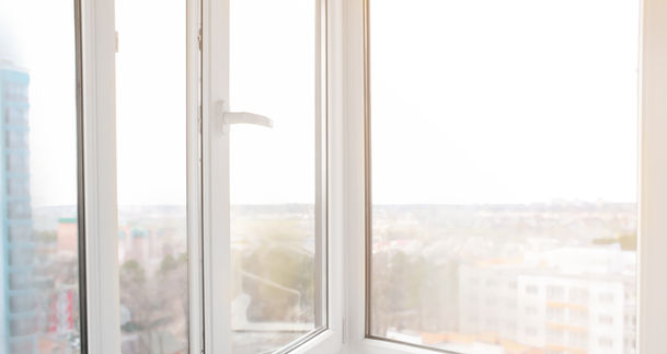 Fenêtre blanche ouverte offrant une vue urbaine lumineuse avec gratte-ciel.