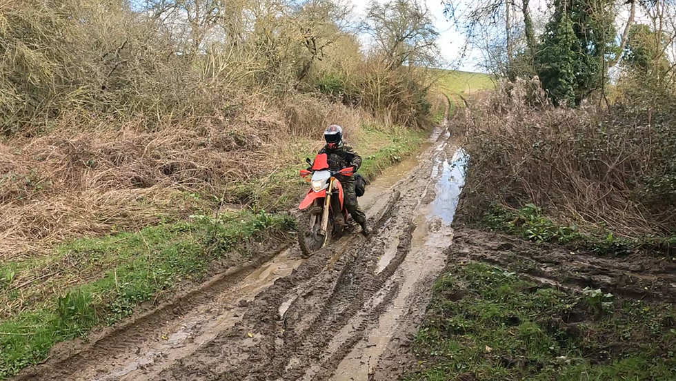 A rider paddles a trail bike through a very muddy puddle.
