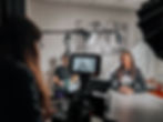 An interview setup, a woman behind a camera filming a woman in front of the camera