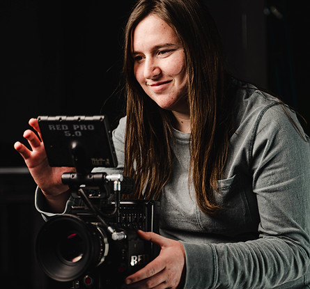 A woman behind a camera and looking at the monitor, smiling