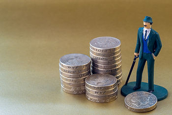 Toy man in green suit and hat stands by stacks of British pound coins on a gold background. Coins have visible text.