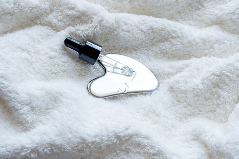 A stainless steel gua sha tool with a pipette lies on a soft towel, close-up.jpg