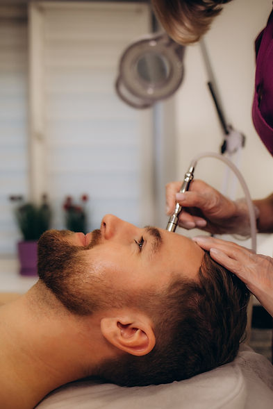 The cosmetologist makes the procedure Microdermabrasion of the facial skin of a man in a b