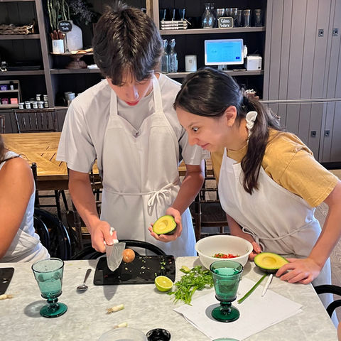 A sister looks at her brother while he prepares guacamole at Violet Cooking School