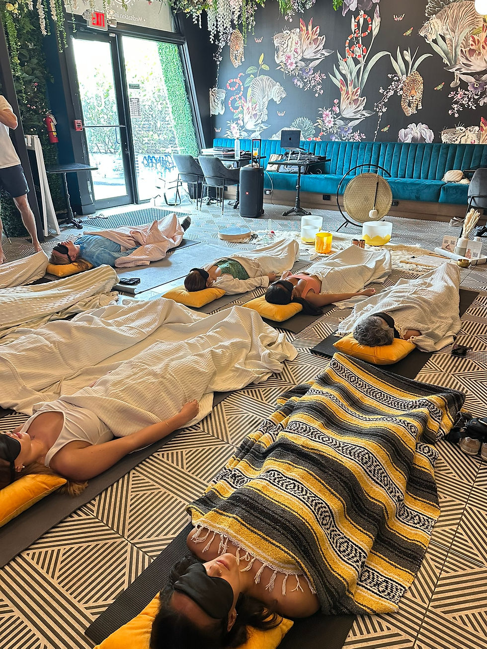 People lying on mats with eye masks, covered in blankets in a room with floral wallpaper. The atmosphere is calm and relaxing.