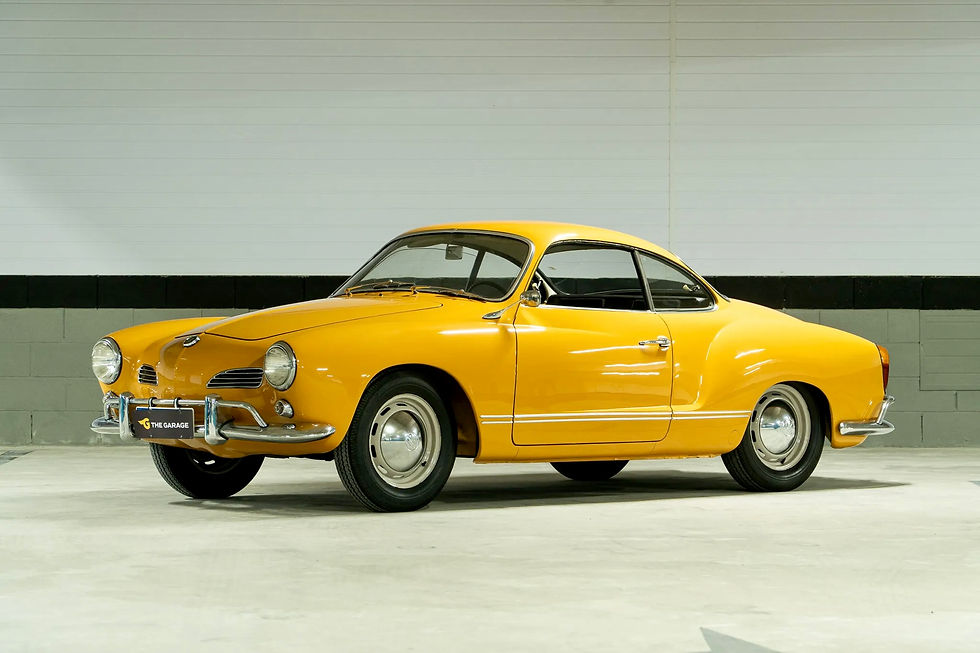 A yellow vintage car parked in a garage with a cream and black wall background. The "THE GARAGE" license plate is visible.