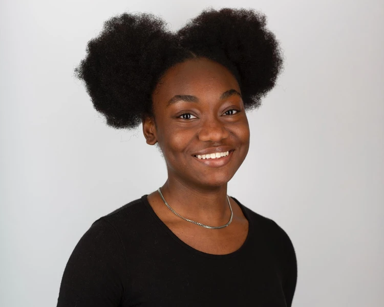 Young lady smiling at camera wearing black dress and hair tied up into two bunches either side of head.