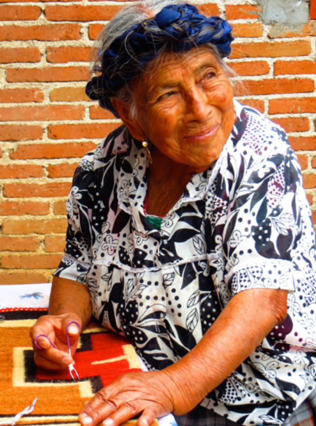 Oaxacan artisan trimming loose threads on woven rug.