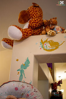 Giant plush giraffe perched above a doorway decorated with glittery mermaid murals
