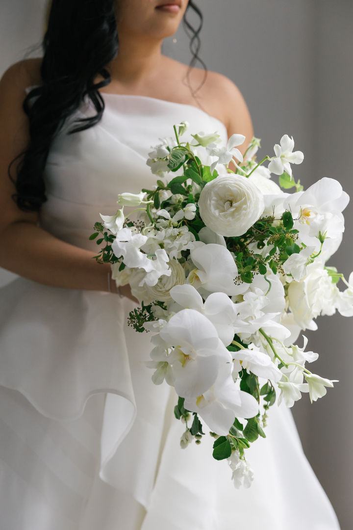 Modern cascading bridal bouquet featuring exquisite white orchids and fluffy ranunculus. Luxurious wedding flowers with abundant texture for a truly unforgettable day. #LuxuryWeddingFlorist #CascadingBouquet #WhiteOrchids #Ranunculus #ModernBridal #WeddingFlowers #BridalBouquetGoals #WeddingInspo #HighEndWedding