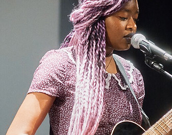 Young Musician with lavender braids sings into a mic, intent on her performance